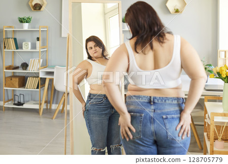 Obese woman mirror looking with excessive belly visceral fat at home trying on jeans, overweight  128705779