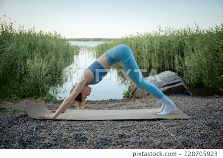 Young woman practicing yoga exercises near a lake in a summer day 128705923