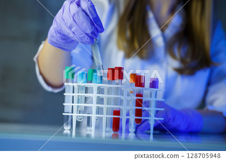 A medical professional, laboratory assistant, doctor performs an analysis in a laboratory, uses test tubes, a pipette and a petri dish for the presence of bacteria in the human body 128705948