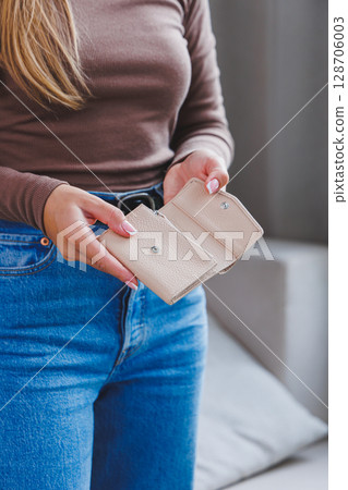 A beautiful woman holds a beige leather purse in her hands. Small women's handbag 128706003