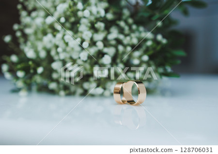 Precious gold rings for newlyweds on a background of flowers. Wedding rings for a couple. Precious gold rings for newlyweds on a background of flowers. Wedding rings for a couple. 128706031