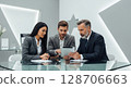 Three business professionals collaborating, analyzing data on a tablet device, discussing strategy. 128706663