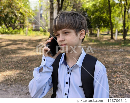 schoolboy boy is holding a mobile phone in his hands, about to call his parents. teenage boy uses his mobile phone on his way to school. back to school. schoolboy boy is holding a mobile phone in his hands, about to call his parents. teenage boy uses his mobile phone on his way to school. back to school. 128706841