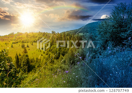 summer landscape with forest on the hill. scenic view of highlands with sun and moon at twilight. day and night time change concept. scenery under dark blue sky and rainbow 128707749