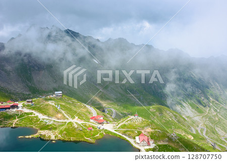 romania travel landscape with road pass. green valley of fagaras mountains. dramatic scenery of transylvania. beautiful view above alpine lake balea in summer. scenic landmark of europe romania travel landscape with road pass. green valley of fagaras mountains. dramatic scenery of transylvania. beautiful view above alpine lake balea in summer. scenic landmark of europe 128707750