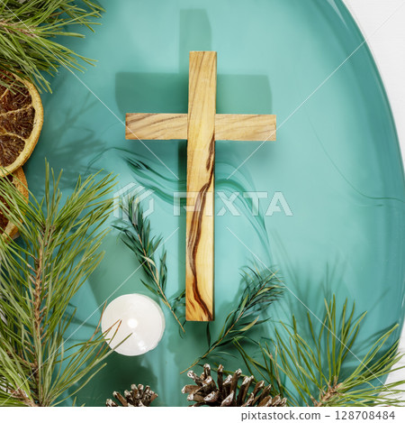 Wood cross laying on a green marble podium with fir branches, cones, candle and dry oranges on a white background. Christmas holidays. Christian religion card. Flat lay Wood cross laying on a green marble podium with fir branches, cones, candle and dry oranges on a white background. Christmas holidays. Christian religion card. Flat lay 128708484