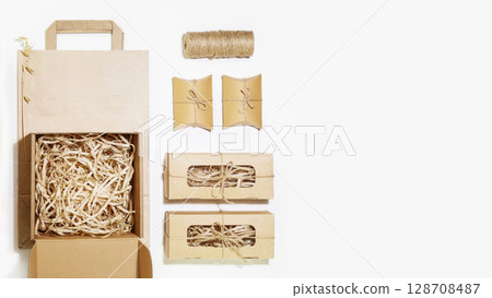 Eco friendly packaging concept. Cardboard boxes with shredded paper inside, paper bag and small gift boxes for packaging goods from online stores and delivery on white background with copy space 128708487