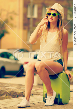 Woman traveler sits on suitcase waiting for car. Woman traveler sits on suitcase waiting for car. 128708844