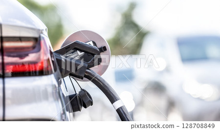 Focus closeup electric vehicle plugged in with EV charger device from blurred background of public charging station powered by renewable clean energy for progressive eco-friendly car concept Focus closeup electric vehicle plugged in with EV charger device from blurred background of public charging station powered by renewable clean energy for progressive eco-friendly car concept 128708849