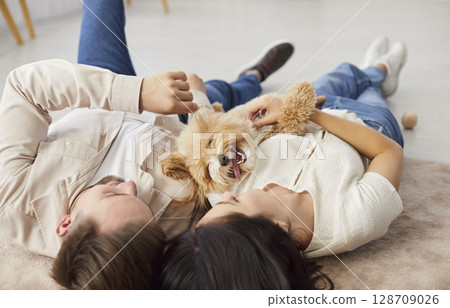 Young couple relaxing on floor with their happy dog, enjoying leisure time together in cozy home. 128709026