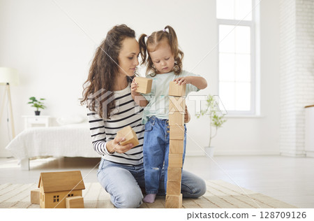 Happy smiling mother and baby daughter, babysitter nanny cube block building game, friendly loving 128709126