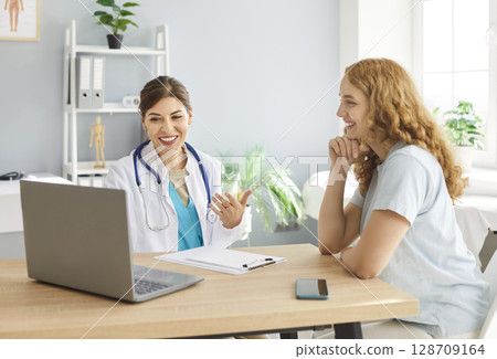 Happy, smiling female doctor and patient are looking at laptop computer at clinic Happy, smiling female doctor and patient are looking at laptop computer at clinic 128709164