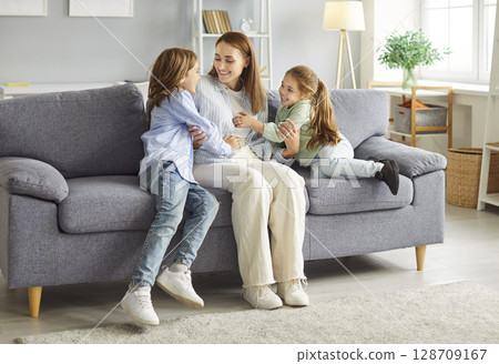Mother spending time with her kids on gray couch in living room, having fun and laughing together. 128709167