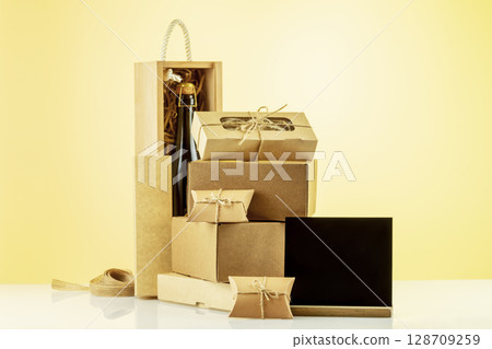 Eco friendly shopping and delivery service. Craft cardboard gift boxes, wooden box with bottle of champagne and empty blackboard on beige background. Zero Waste, plastic free, eco packaging concept Eco friendly shopping and delivery service. Craft cardboard gift boxes, wooden box with bottle of champagne and empty blackboard on beige background. Zero Waste, plastic free, eco packaging concept 128709259