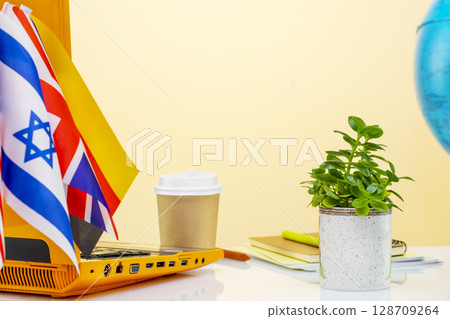 International online education. Laptop, notebooks, a globe, a cup of coffee and flags of different country on a beige background with copy space. Concept of E learning and distance education International online education. Laptop, notebooks, a globe, a cup of coffee and flags of different country on a beige background with copy space. Concept of E learning and distance education 128709264