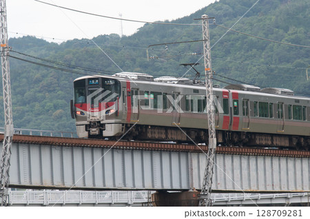 【廣島可部線】JR227系列車(紅翼號)在青山環繞的鐵橋上行駛 【廣島可部線】JR227系列車(紅翼號)在青山環繞的鐵橋上行駛 128709281