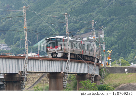 [Hiroshima Kabe Line] JR 227 Series train (Red Wing) running on a railway bridge with green mountains in the background 128709285