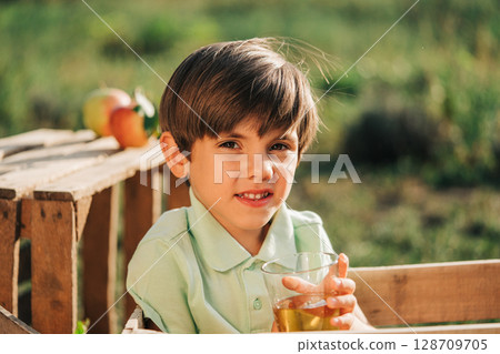 Cute little toddler boy drinking apple juice. Child in wooden box in orchard. 128709705