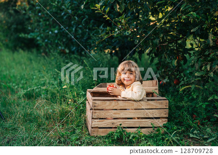 Funny little boy eating juicy apple,sitting in wooden box orchard.Organic fruits 128709728