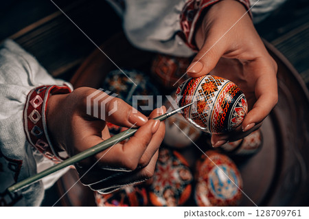 Ukrainian woman painting traditional ornamets on Easter egg - pysanka.  128709761