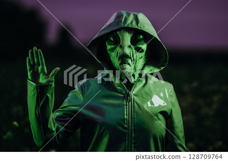 Spooky alien waving hello, hi, salute in field under green neon light. Scary mask, vinyl smooth Spooky alien waving hello, hi, salute in field under green neon light. Scary mask, vinyl smooth 128709764