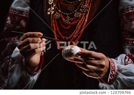 Ukrainian woman painting traditional ornamets on Easter egg - pysanka.  128709766