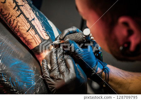 Tattooist doing tattoo for client with machine close-up.Getting tattoo in parlor Tattooist doing tattoo for client with machine close-up.Getting tattoo in parlor 128709795