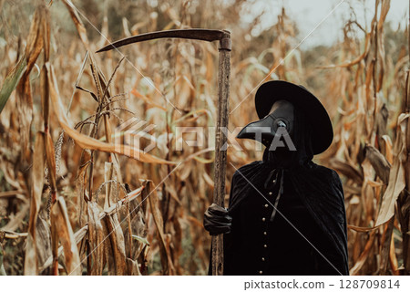 Plague doctor gothic woman with sharp scythe standing in autumn thickets of corn 128709814