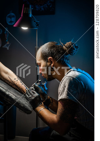 Man tattoo master with dreadlocks showing process creation tattoo, female body  128709820