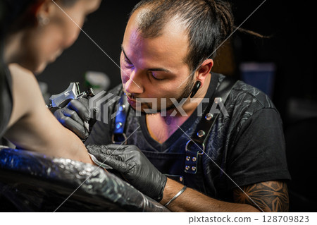 Man tattoo master with dreadlocks showing process creation tattoo, female body  128709823