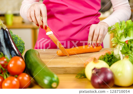 Woman cutting carrot on kitchen board Woman cutting carrot on kitchen board 128710054