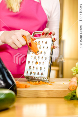 Woman grating carrot on metal grater Woman grating carrot on metal grater 128710065