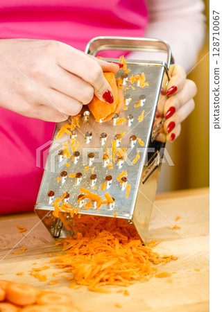 Woman grating carrot on metal grater 128710067