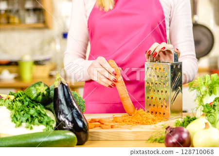 Woman grating carrot on metal grater 128710068