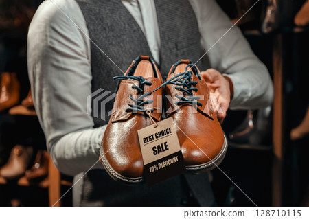 Salesman Holding Brown Leather Shoes with Discount Tag 128710115