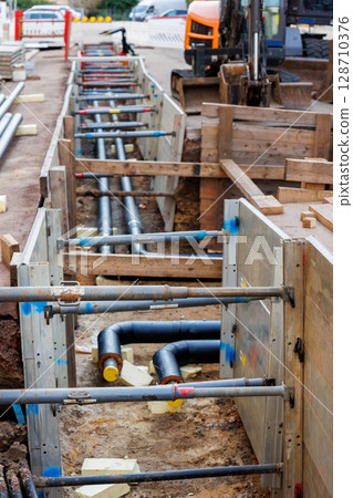 New modern insulated urban pipeline installation construction site  exposed underground pipes in shored trenches. Insulated steel pipes lie connection engineering infrastructure upgrade work 128710376