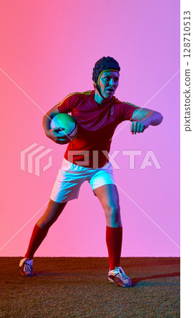 Woman rugby athlete posing dynamically against vibrant gradient backdrop Woman rugby athlete posing dynamically against vibrant gradient backdrop 128710513