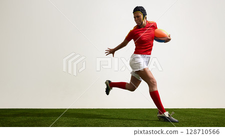 Female rugby player running with ball against white background 128710566