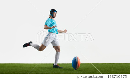Female rugby player striking a ball on grassy field with dynamic movement Female rugby player striking a ball on grassy field with dynamic movement 128710575