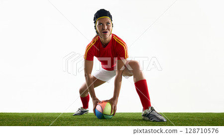 Rugby athlete in red attire stands ready with vibrant ball on green field Rugby athlete in red attire stands ready with vibrant ball on green field 128710576