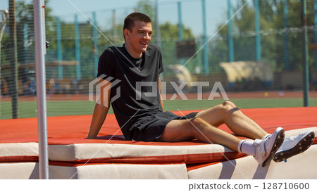 Athlete taking a break on high jump mat at sunny outdoor sports track Athlete taking a break on high jump mat at sunny outdoor sports track 128710600