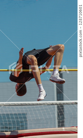 Athlete executes high jump above bar beneath clear blue sky Athlete executes high jump above bar beneath clear blue sky 128710601