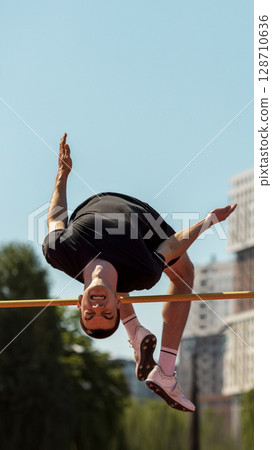 Athlete midair executing high jump at outdoor track and field event 128710636