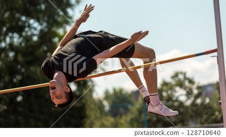 Athlete airborne in high jump at outdoor competition Athlete airborne in high jump at outdoor competition 128710640