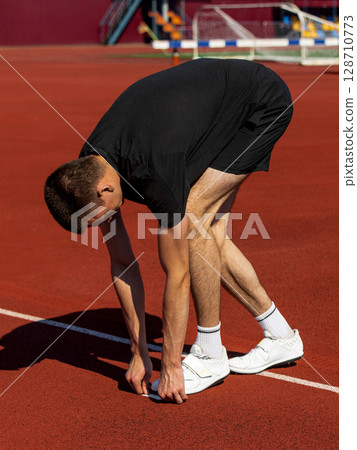 Athlete preparing with stretches on track beneath sunny sky before run Athlete preparing with stretches on track beneath sunny sky before run 128710773