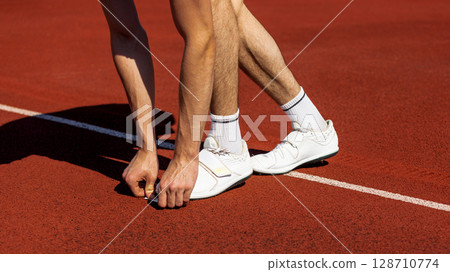 Athlete in starting stance on red track surface under bright sunlight preparing to sprint Athlete in starting stance on red track surface under bright sunlight preparing to sprint 128710774