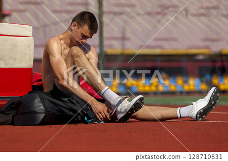 Athlete lacing up shoes on running track under sunny sky 128710831