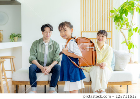 一個背著書包的女孩，她的父母在一旁看著 128711612