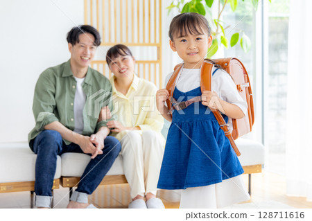 A girl carrying a school bag, her parents watching A girl carrying a school bag, her parents watching 128711616
