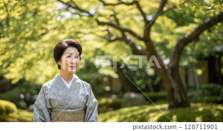 Elegant senior japanese woman in a traditional kimono smiling serenely in a lush green garden 128711901